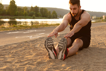 Young athletic man stretching his legs after workout near cycle lane at the river bank
