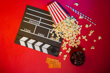 Cinema concept. Clapperboard, ticket and popcorn on red background