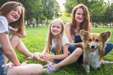 mother with her daughters and dog are sitting on a grass