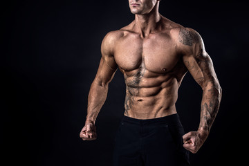 Unrecognizable Strong bodybuilder with six pack. Bodybuilder man with perfect abs, shoulders,biceps, triceps and chest, personal fitness trainer flexing his muscles ob black, dark background in studio