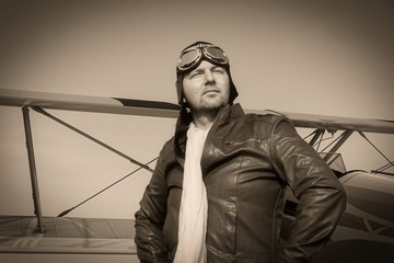 Portrait of a vintage pilot with leather cap, scarf and aviator glasses in front of a historic...