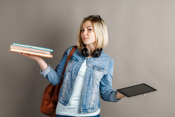Book vs. e-book. Girl student holding a traditional textbook and reading e-books isolated on gray...