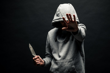 Dangerous man in the hood stands in the dark and holds a knife. The face is not visible. The...