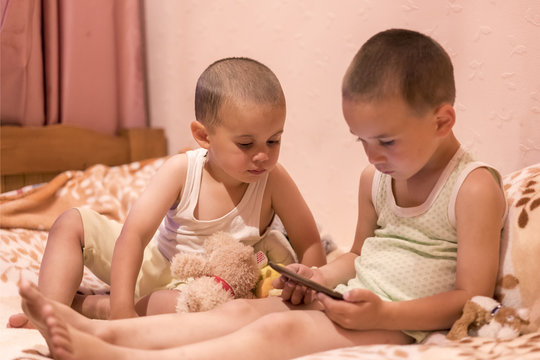 children in the bedroom watching cartoons. children play on smarfone. two brothers in the bedroom look at the smartphone. toned