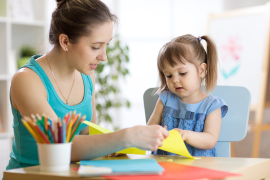 Mother helping her child daughter to cut colored paper