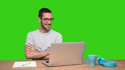 Satisfied young man sitting at his desk - Green background