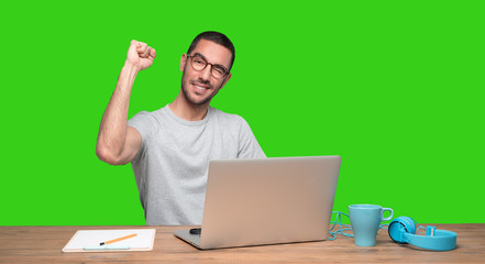 Happy young man sitting at his desk with a gesture of celebration - Green background.