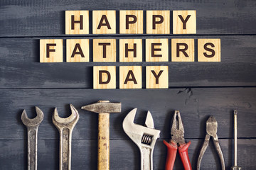 Happy Father's Day inscription on wooden cubes with working tools on a wooden background. Greetings and gifts.