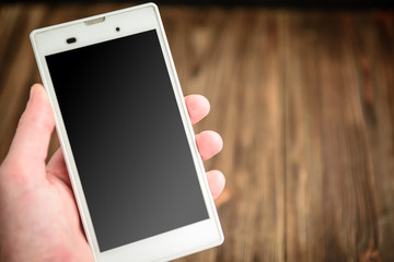Hand holding phone mobile blank screen. Smart phone on wooden table background with copy space.