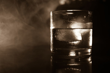 selective focus pure whisky with ice cube inside whisky glass on dark foggy background alcohol drink concept.