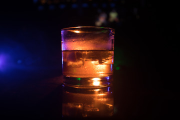 selective focus pure whisky with ice cube inside whisky glass on dark foggy background alcohol drink concept.