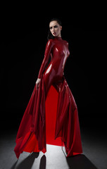 Brunette woman in red latex slim suit posing on dark background