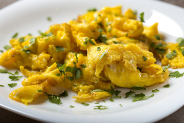 Scrambled eggs on a white plate with green parsley