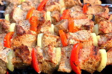 Pieces of juicy slices of marinated pork meat strung on skewers with slices of chopped tomatoes and onion cooking on the grill. Cooking shashlik on the brazier Close-up.