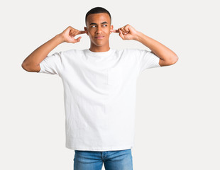 Young african american man covering both ears with hands on isolated background