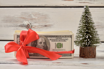 Dollars with red ribbon bow. Money gift and christmas tree.