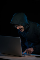 Hacker in a dark hoody sitting in front of a notebook. Computer privacy attack