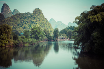 Fototapeta na wymiar Scenic view of Yulong River among green woods and karst mountains at Yangshuo County of Guilin, China. Yangshuo is a popular tourist destination of Asia.