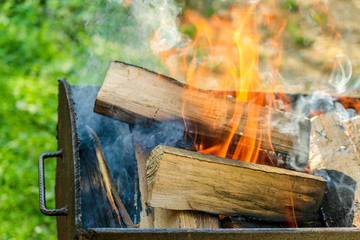 Barbecue with burning firewood. Big firewood burning in the iron grill with smoke and flame. Outdoors.