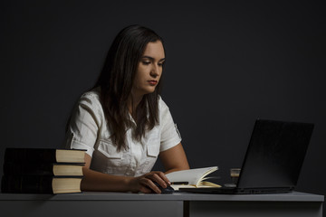 A girl uses a laptop and writes something to a notebook