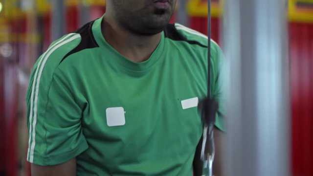 Tilt up of focused Arab man training triceps on cable pushdown machine in gym, then shaking his head and laughing