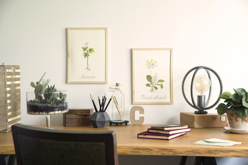 Vintage, creative home office interior with wooden desk, books, laptop, romantic illustrations of plants, lamp and office accessories.
