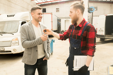 Young bearded auto mechanic giving car keys to happy male client after successful inspection of his vehicle in service garage