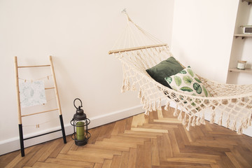 Modern and stylish bedroom with natural string hammock, plants and shelves with accessories. Bright...