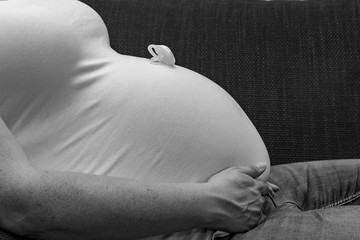 Small pacifier on the top of a belly button of a pregnant woman as black and white photo