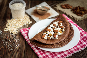 Homemade chocolate oat pancake with cottage cheese on white plate on dark wooden table.