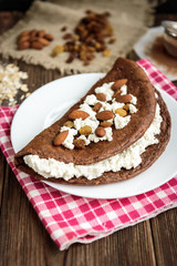 Homemade chocolate oat pancake with cottage cheese on white plate on dark wooden table.