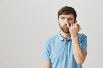 Can I dig to brain. Studio shot of clueless untidy caucasian guy looking aside with confused expression, picking in nose with pinky, thinking nobody sees him over gray background. - obrazy, fototapety, plakaty