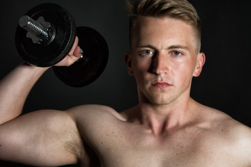 Fototapeta na wymiar Gym and dumbbells. Young attractive guy. Black background. 