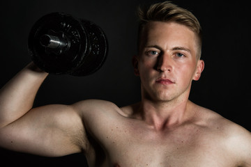 Fototapeta na wymiar Gym and dumbbells. Young attractive guy. Black background. 