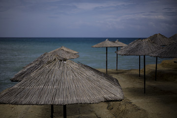 Beach resort under construction with wooden umbrellas which is very near to beach. The floor is made of beach sand and in the background there is turquoise sea  and the dull blue sky.