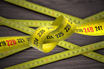  Tangled metal tape measure above wooden table close up 
