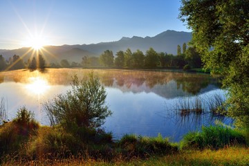 Sonnenaufgang an einem Teich mit Spiegelung auf der Wasseroberfläche