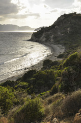Fototapeta na wymiar Landscape of romantic summer evening by the sea. Seascape of small waves on sea, empty sand beach, hills with green dune vegetation and mountains on horizon.
