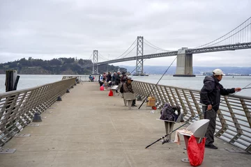 Abwaschbare Fototapete Stadt am Wasser Fishermen on the quay, view of the San Francisco Bridge, USA