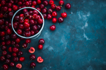 Cherries with a small metal bucket on a grey concrete background, summer berries concept with copy space. Neutral color tones still life