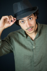 A nice young man, 20Y, is posing in studio with a hat. Black background.