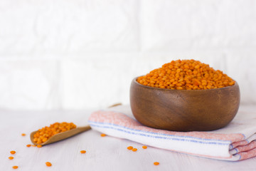 Raw red lentils in a wooden bowl and spoon on a linen napkin on a white table
