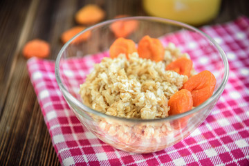 Oatmeal porridge with dried apricot, raisins and honey in bowl on dark wooden background. Healthy food for breakfast.