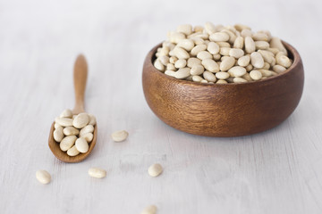Raw white beans in a wooden bowl and spoon on a linen napkin on a white table