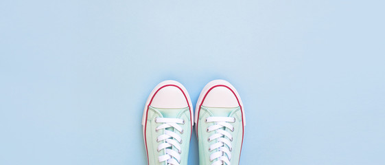 Pastel turquoise female sneakers on blue background. Flat lay, top view minimal background. Fashion blog or magazine concept.