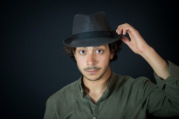 A nice young man, 20Y, is posing in studio with a hat. Black background.