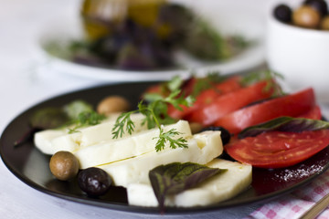 White cheese with tomatoes, green and black olives, basil, coriander and olive oil on a black plate