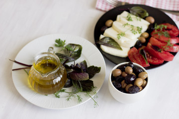 White cheese with tomatoes, green and black olives, basil, coriander and olive oil on a black plate