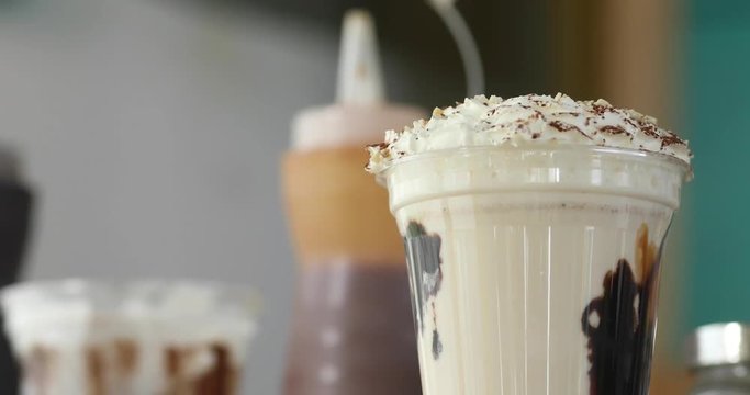 Plastic cup with served milkshake and topping on table with ingredients and sweets