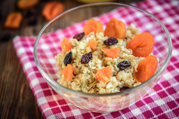 Oatmeal porridge with dried apricot, raisins and honey in bowl on dark wooden background. Healthy food for breakfast.